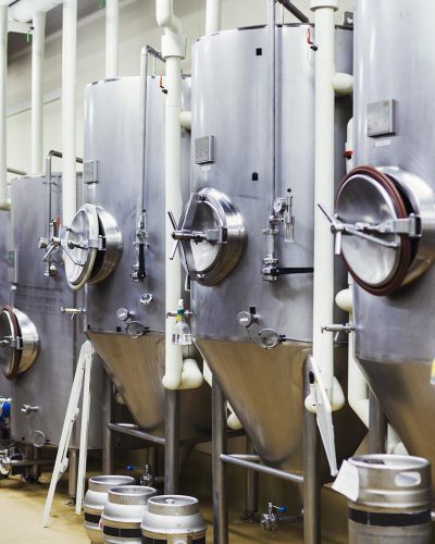 Row of large metal beer tanks in a brewery.